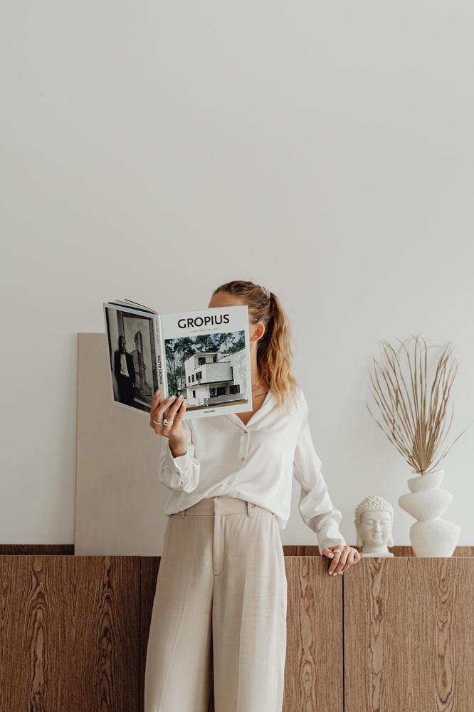 Frau liest in einem Buch und lehnt an einem Sideboard in minimalistischer Wohnung
