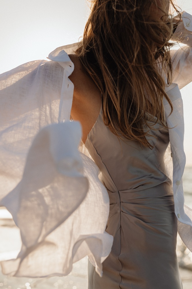 Frau mit beigem Kleid und offenem Leinenhemd steht im Wind, bereit für das Mentoring das ihr Business verändern wird