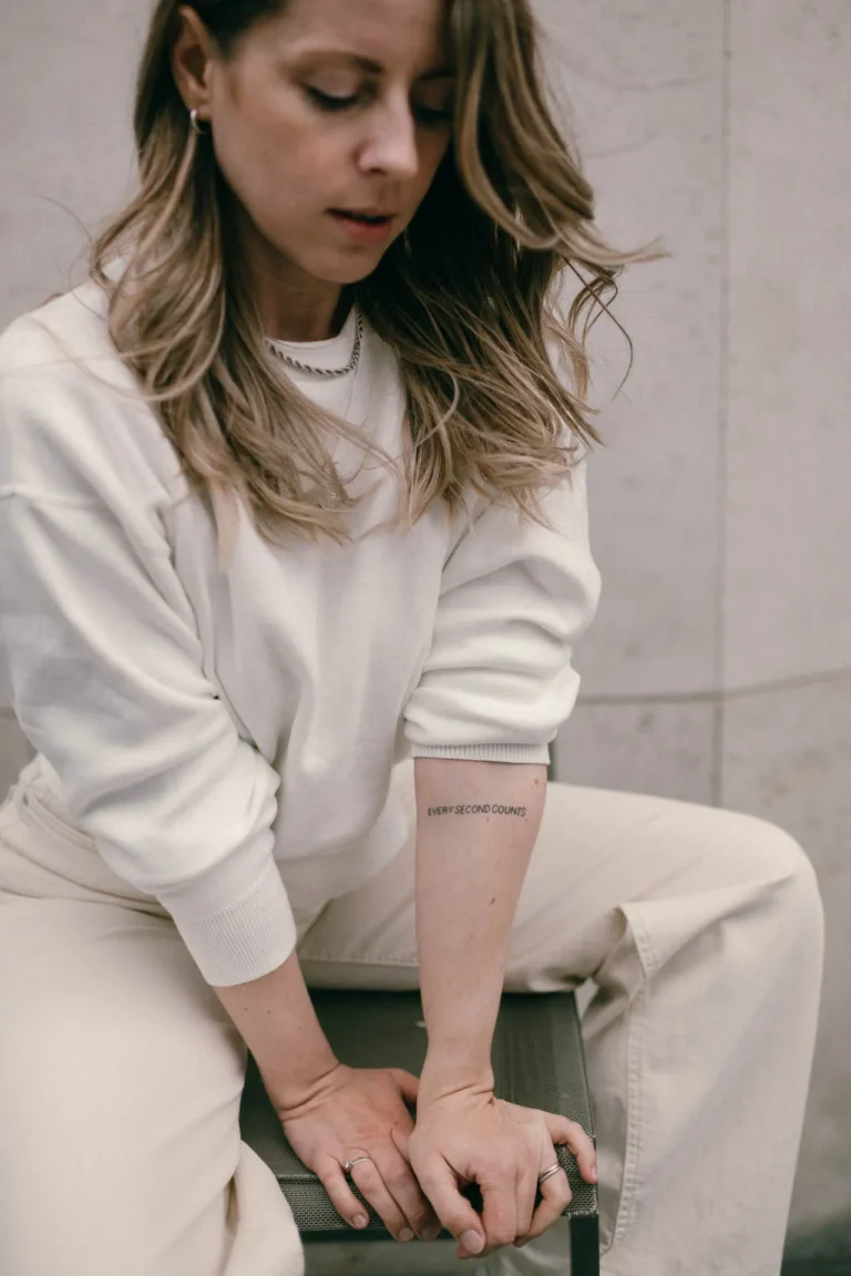 Portrait von Multipreneur Julia Leifheit sitzend auf einem Hocker mit beigem Pulli und Blick nachdenklich nach unten