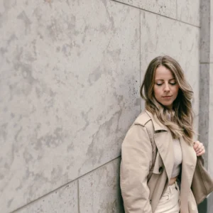 Portrait von Julia Leifheit, Mentorin für Zeitmanagement und Multipreneure, Julia lehnt an der Wand und trägt beige Hose und beigen Blazer
