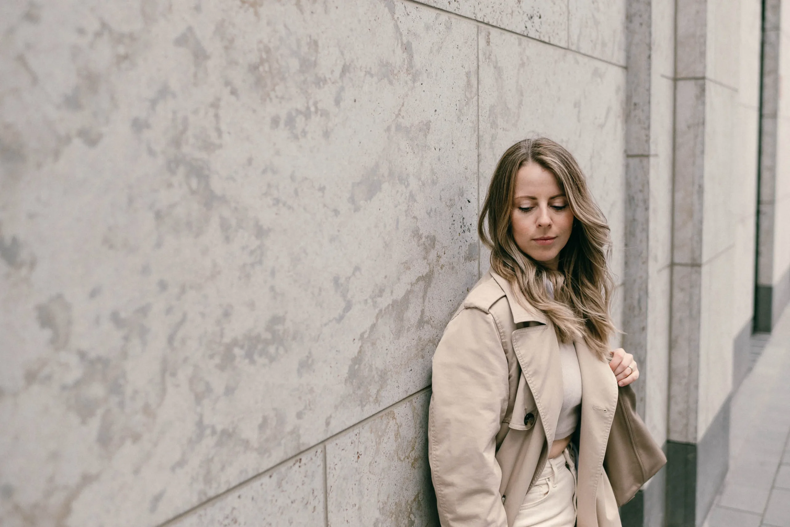 Portrait von Julia Leifheit, Mentorin für Zeitmanagement und Multipreneure, Julia lehnt an der Wand und trägt beige Hose und beigen Blazer