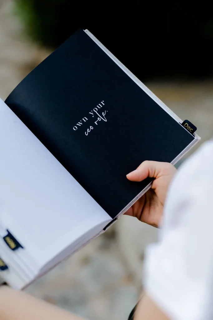 Close-Up vom Zeitmanagement Notizbuch von Julia Leifheit, aufgeschlagen mit einer schwarzen Seite, wird in der Hand gehalten von einer Freu